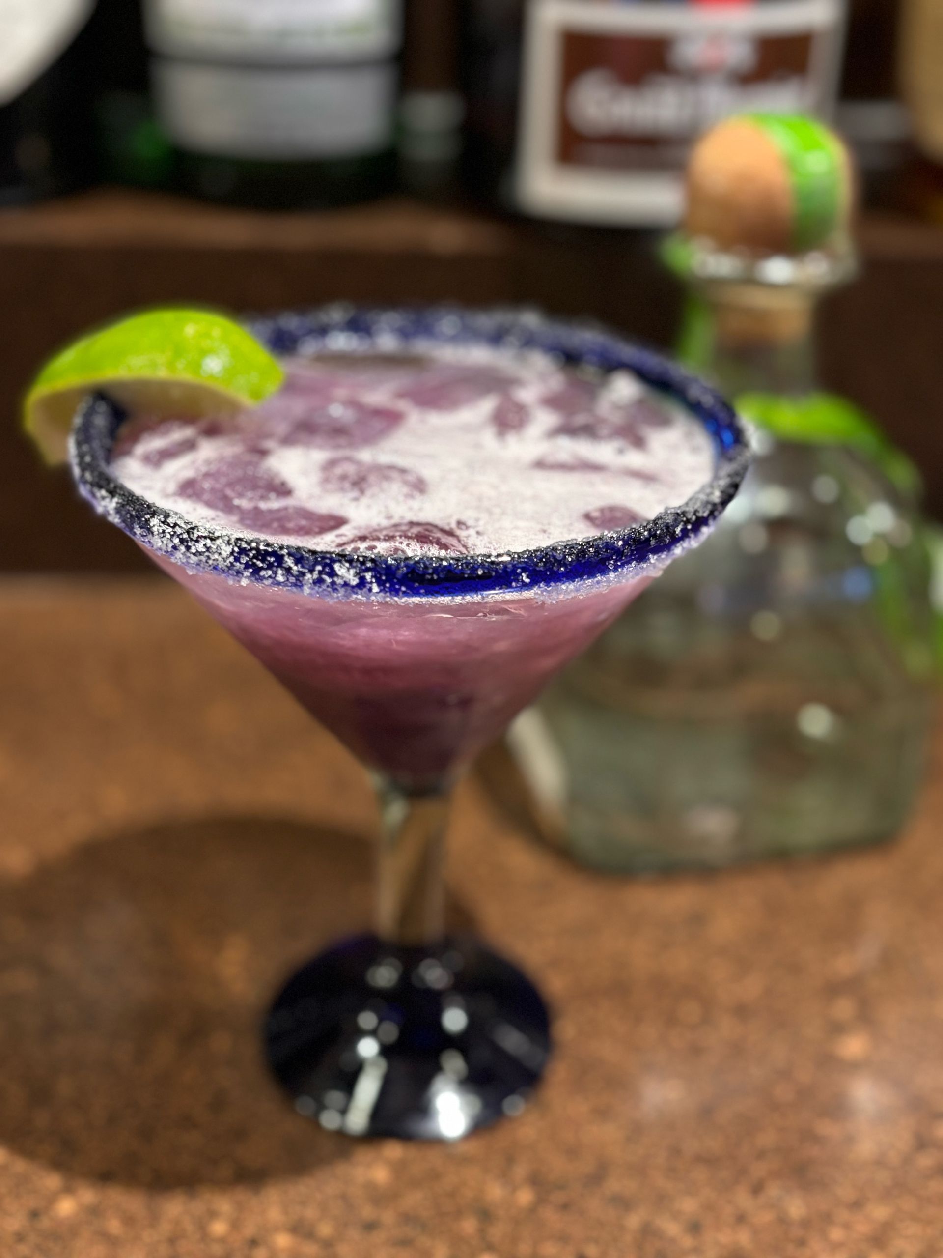 A purple margarita in a martini glass with a blue rim