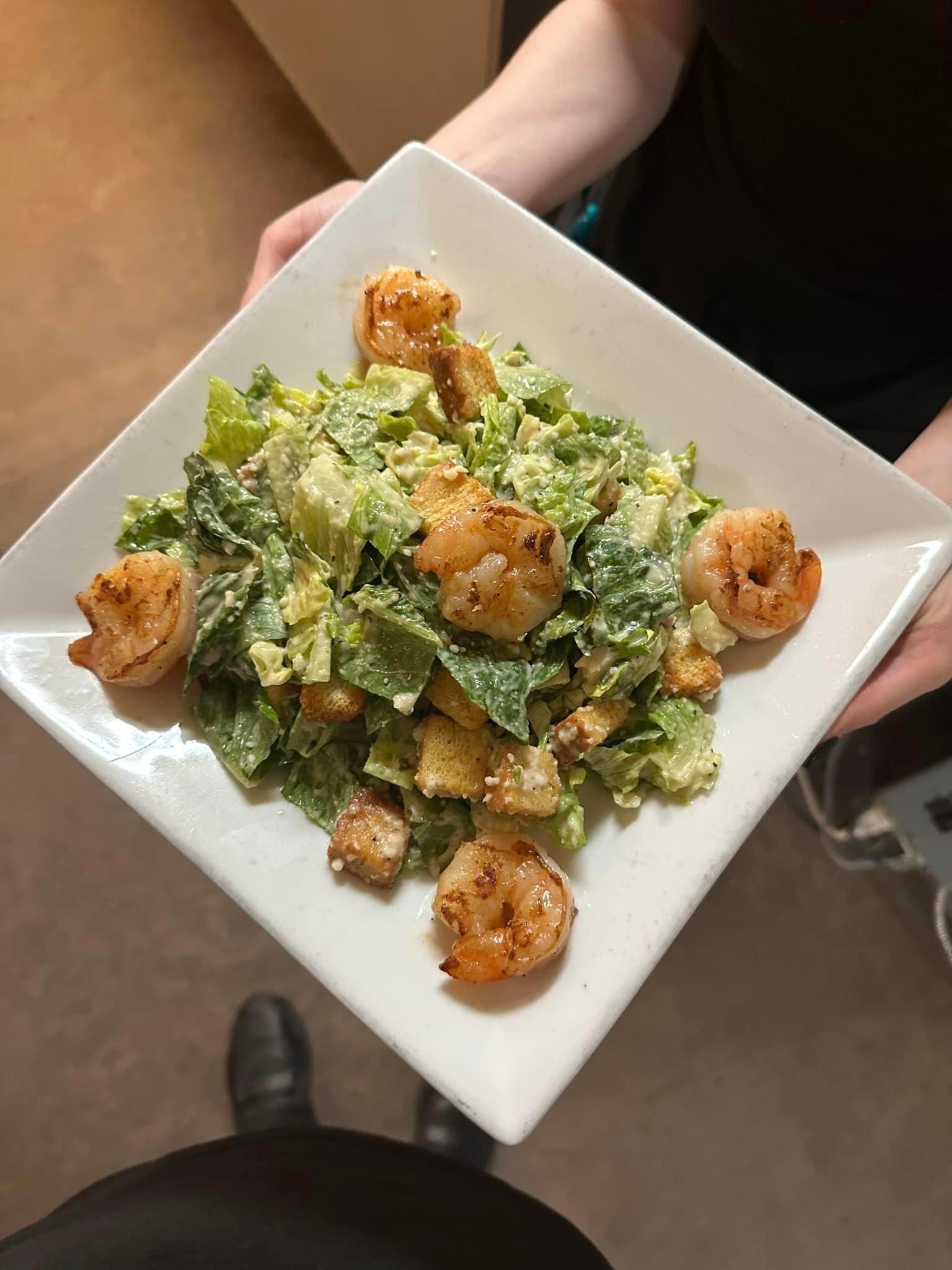 A person is holding a plate of food with shrimp and lettuce.