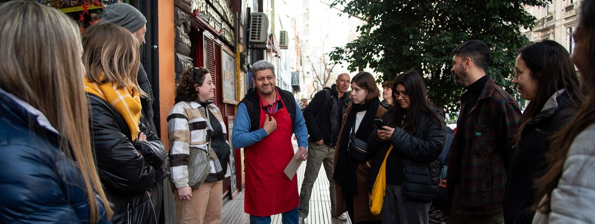 A group of tourists stands close to Beto, an empanada maker from San Telmo. He's wearing a red apron