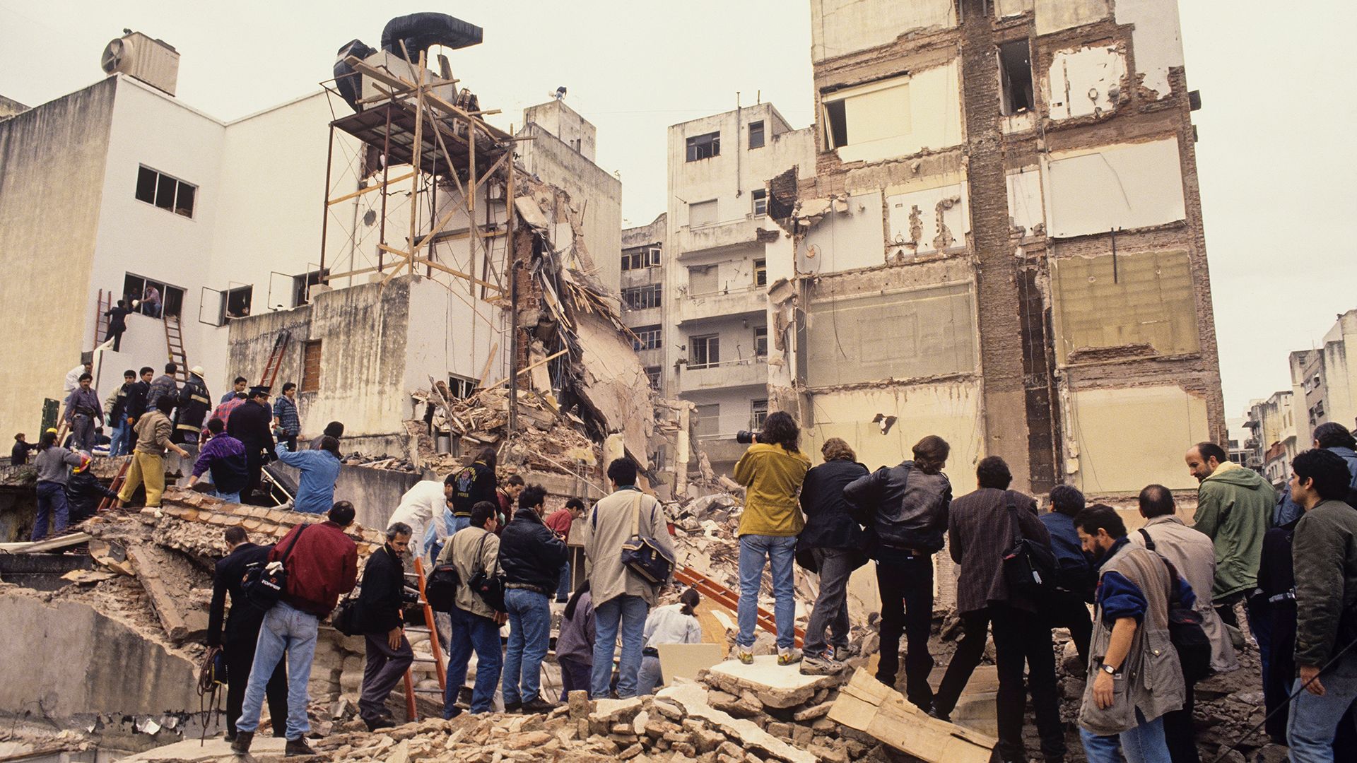 a group of people stands on top of the debris of AMIA