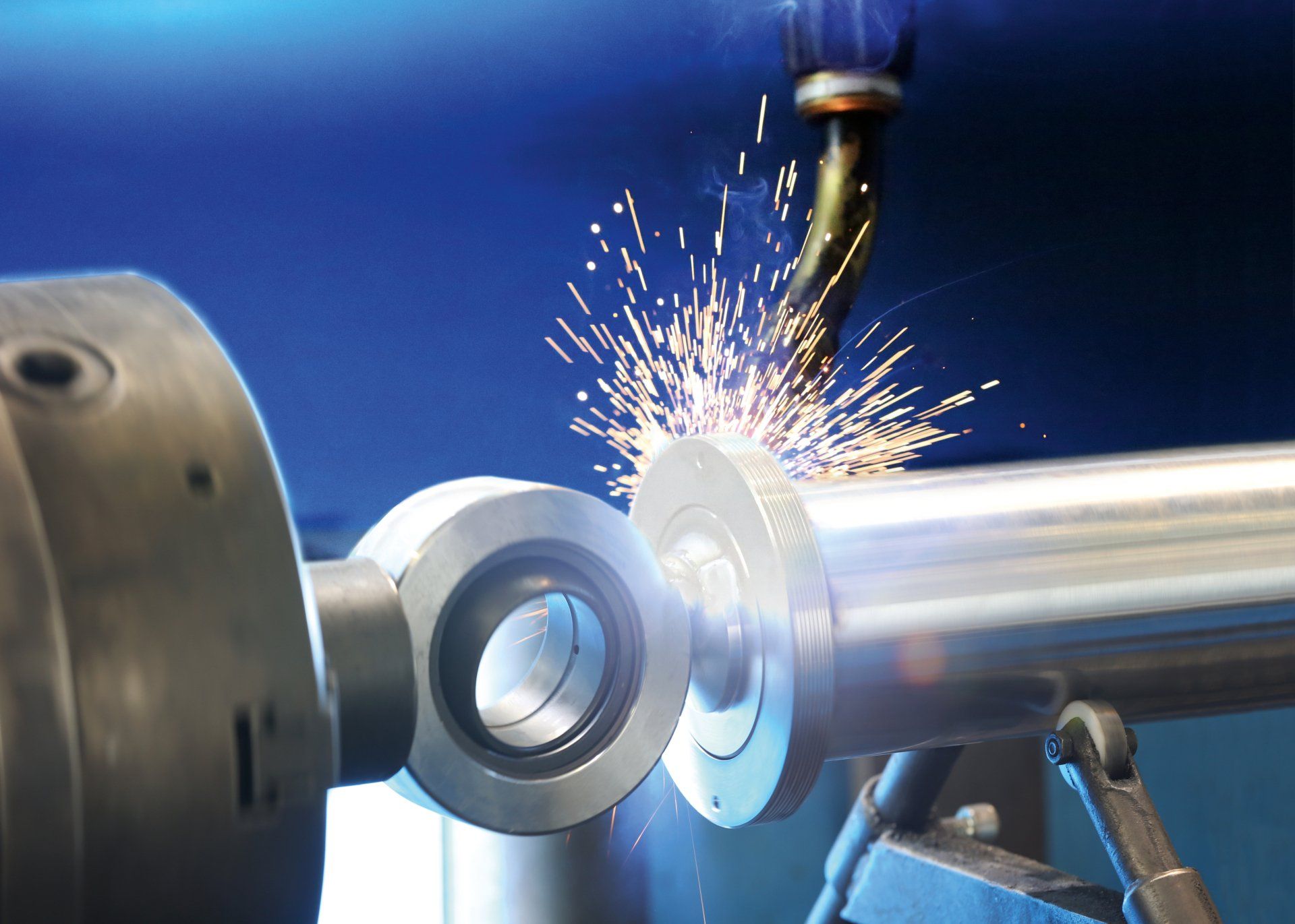 Frau in blauem Hemd und Schürze arbeitet lächelnd an einer Werkbank in einer Fabrik.