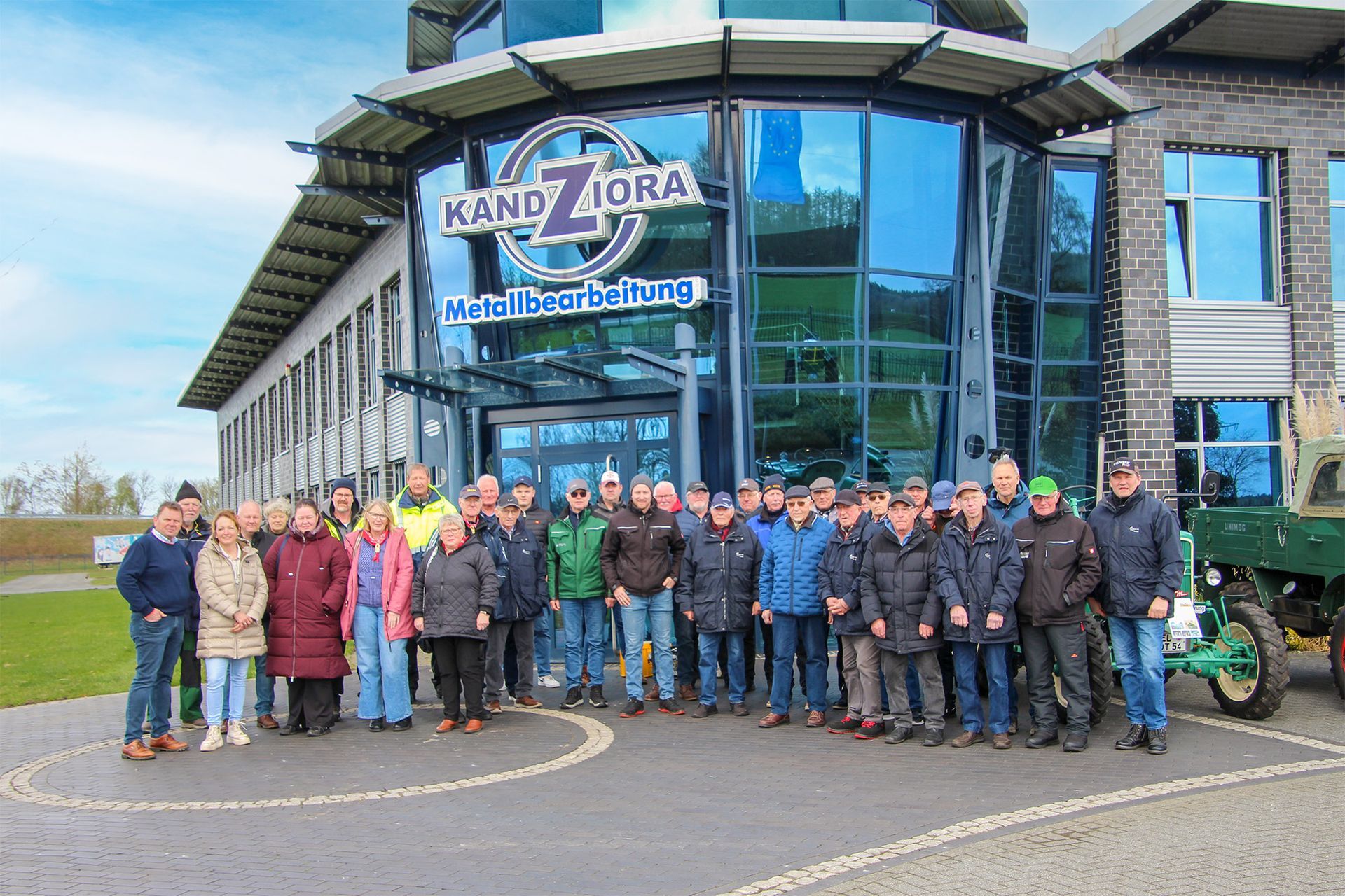 An einem sonnigen Tag steht eine große Gruppe vor dem Gebäude der 