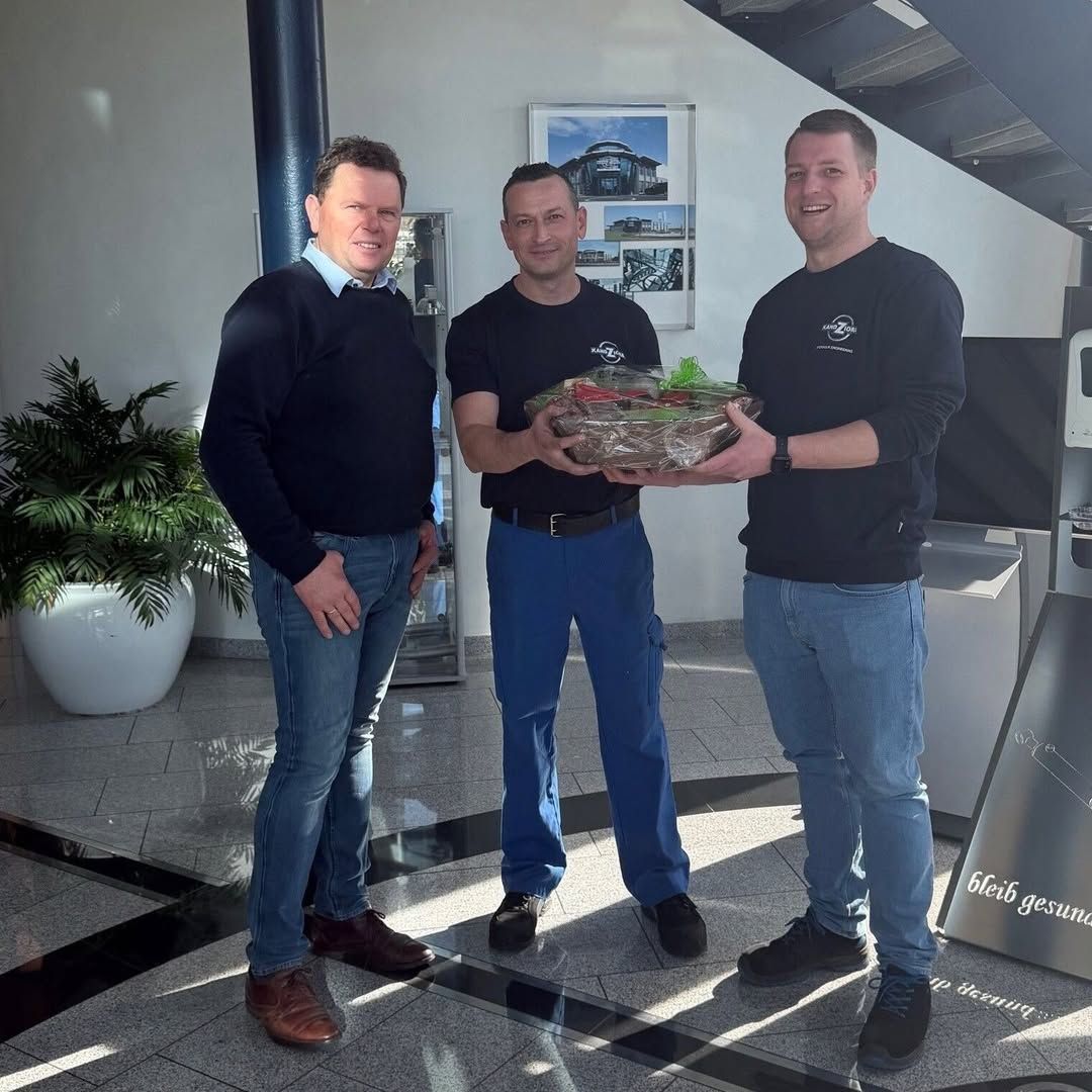 3 Männer stehen nebeneinander und überreichen zum 15. Jubiläum einen Präsentkorb