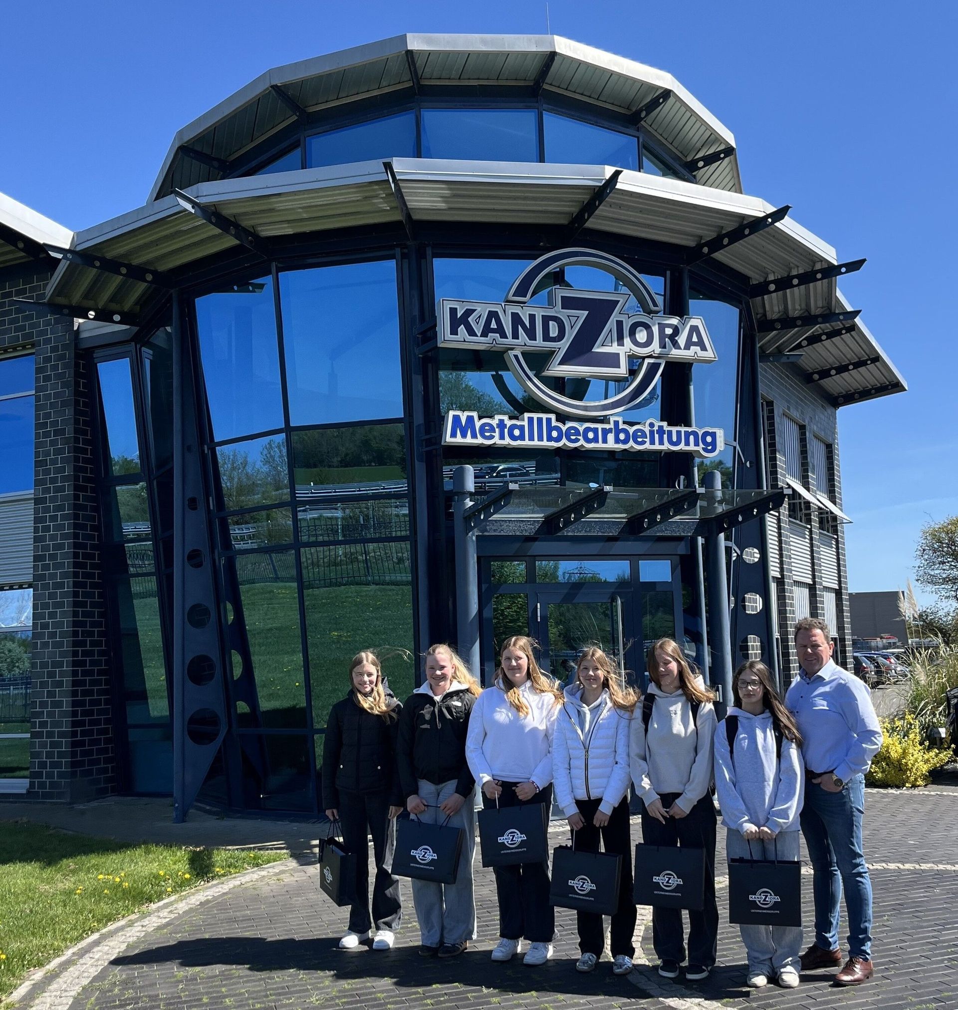 Eine Gruppe von Menschen steht an einem sonnigen Tag vor dem Gebäude von Kandziora