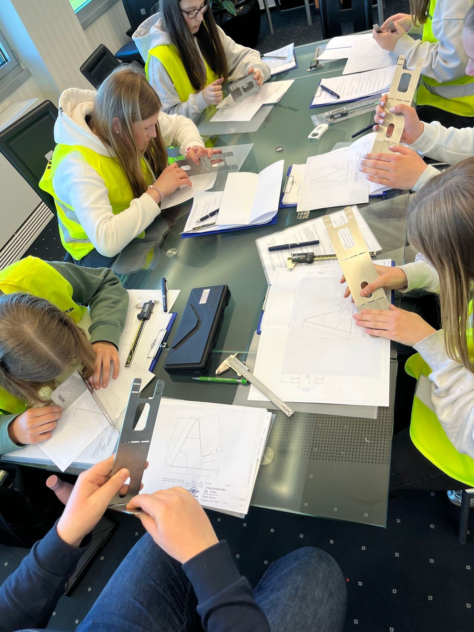 Menschen, die um einen Tisch herum sitzen und auf Papier schreiben, mit Textmarkern und Laptops in der Nähe.