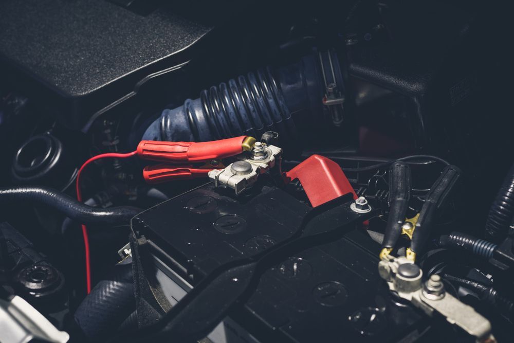 Car battery with red jumper cables attached to terminals. — H & E Auto Electrics in Noosaville, QLD