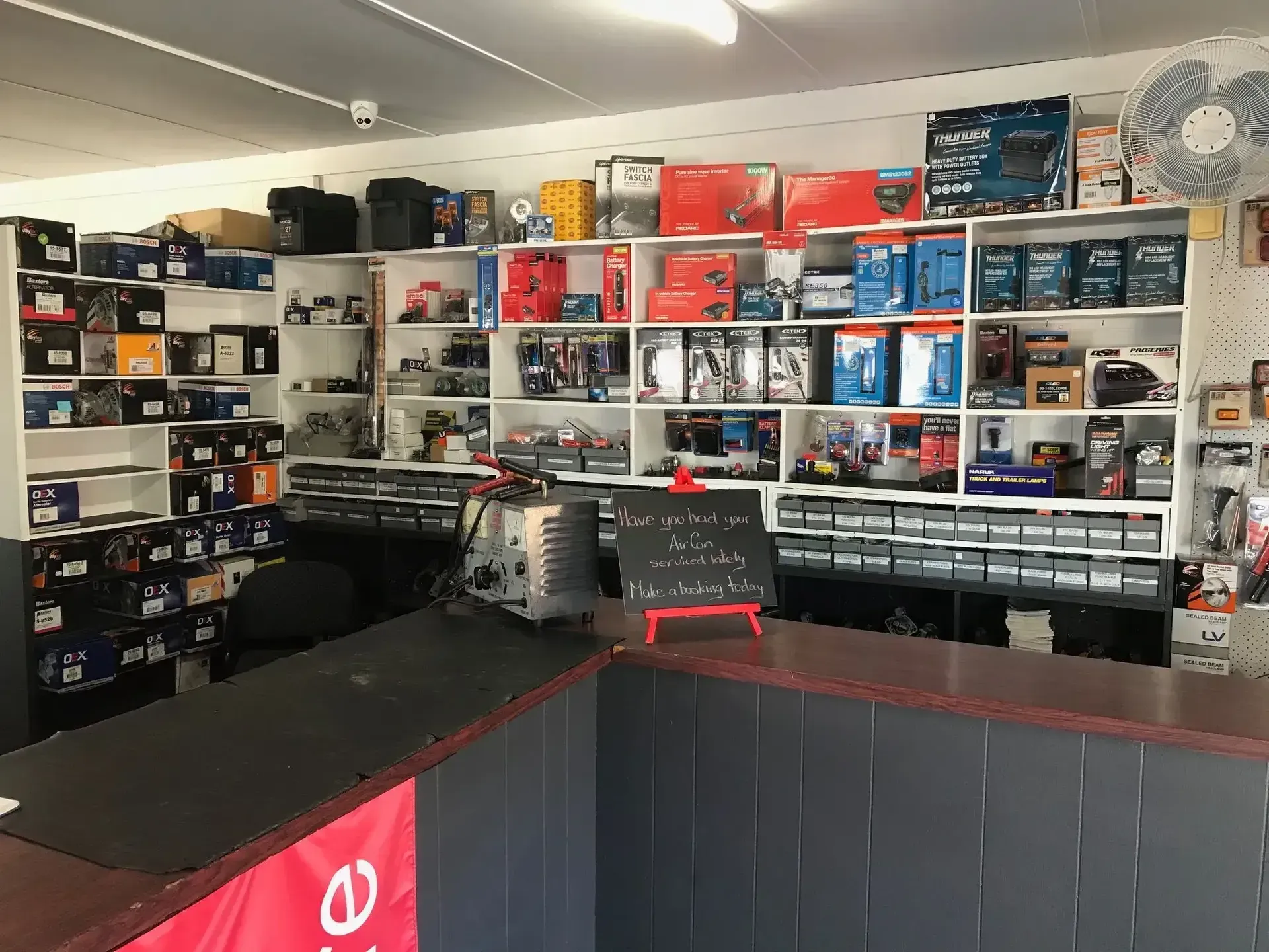 Interior of a store selling car parts. Shelves stocked with boxes, counters, and a small sign. — H & E Auto Electrics in Noosaville, QLD