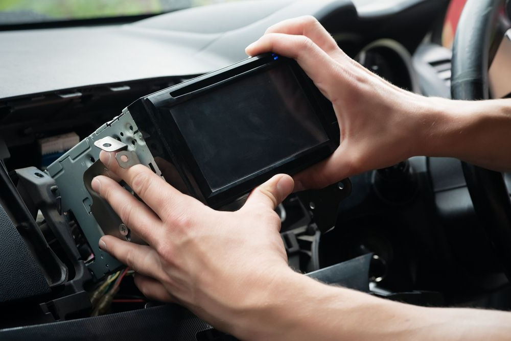 Hands Installing a Car Stereo in a Vehicle's Dashboard — H & E Auto Electrics in Noosaville, QLD
