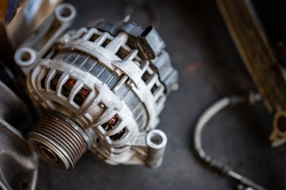 Car alternator with pulley, wires, and mounting brackets, on a dark surface. — H & E Auto Electrics in Noosaville, QLD