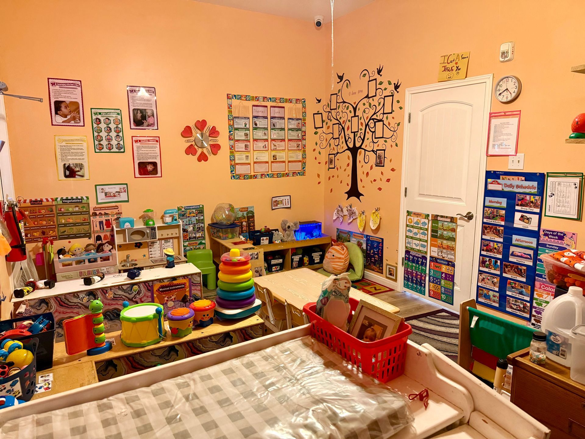 A classroom with a table , chairs , shelves and a ceiling fan.