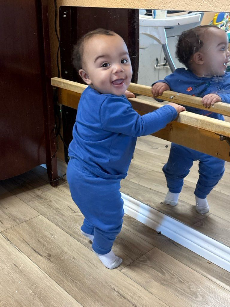 A baby is standing in front of a mirror.