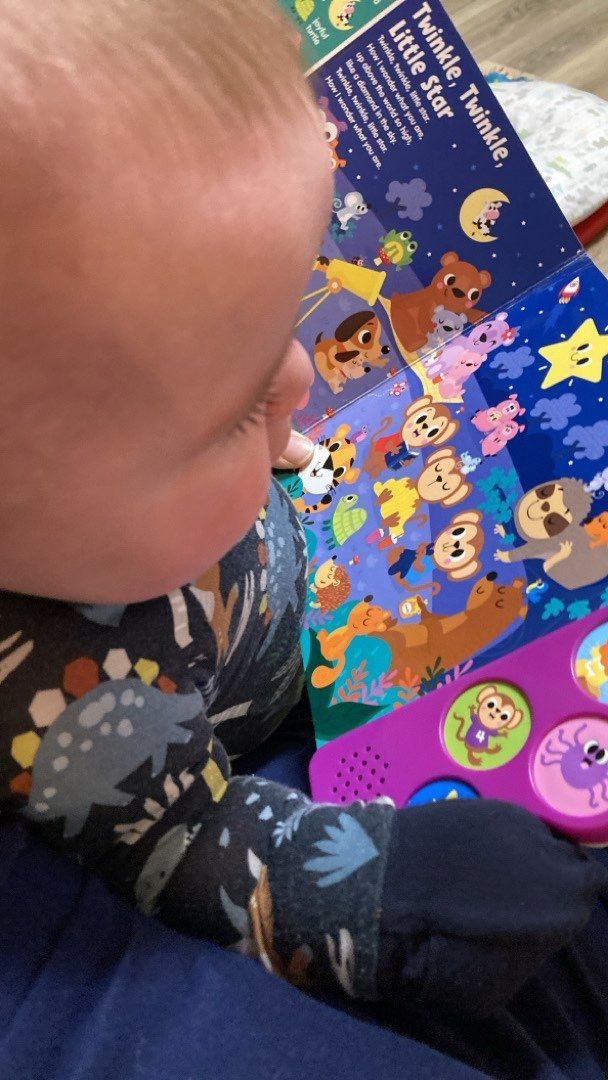 A baby is looking at a book with animals on it.