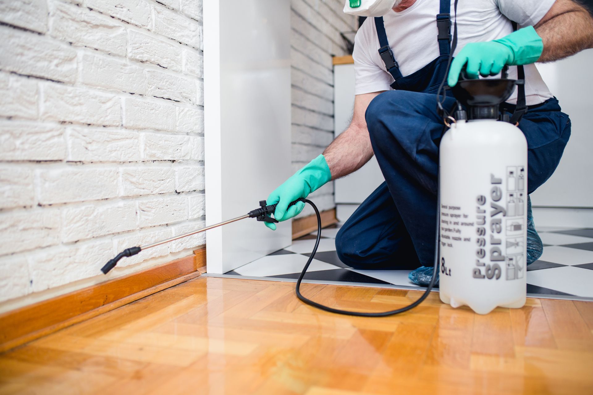 A pest control worker in uniform sprays pesticide with a sprayer.