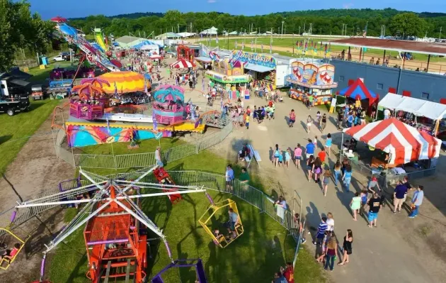 Aerial view of a colorful carnival midway with rides, tents, and crowds walking on a sunny day