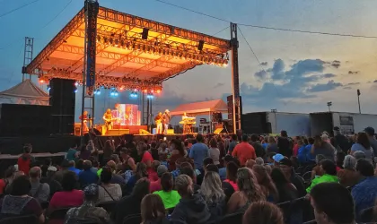 Outdoor concert at dusk with a lit stage and a crowd gathered in front