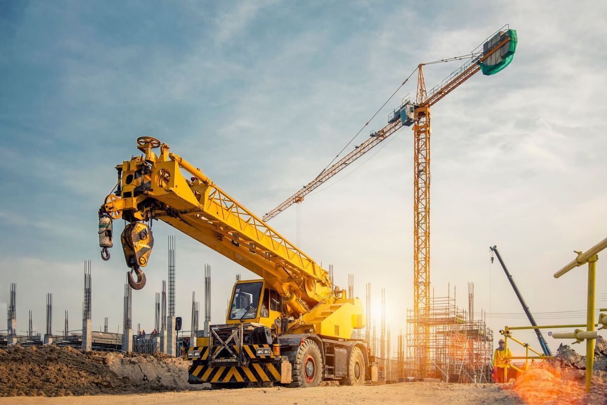 Yellow construction crane on a sunny construction site, with another crane in the background.