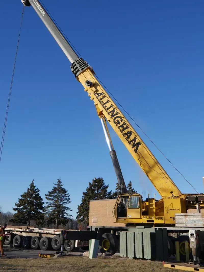 Yellow crane lifting objects from a trailer on a sunny day.