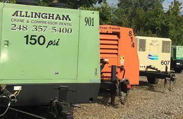 Several air compressors of different colors on trailers, outdoors. The green one has rental info, the orange one has a number 814.