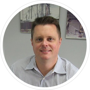 Man in a checkered shirt smiles at the camera in front of neutral-toned artwork, indoors. Man in a checkered shirt smiles at the camera in front of neutral-toned artwork, indoors.
