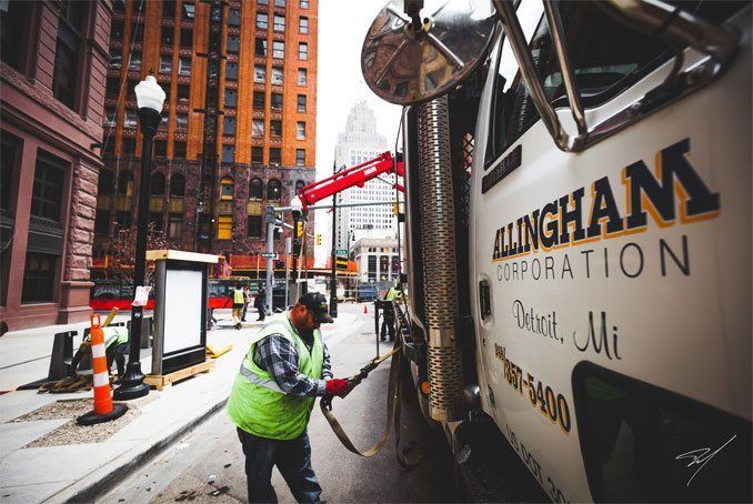 Construction worker attaches equipment to a truck in a city setting.