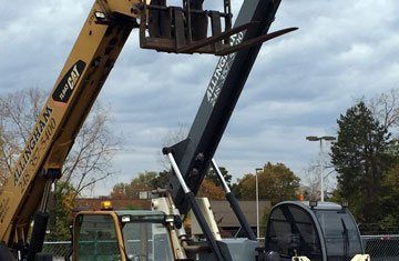 Yellow and black telehandler with forks extended against a cloudy sky.