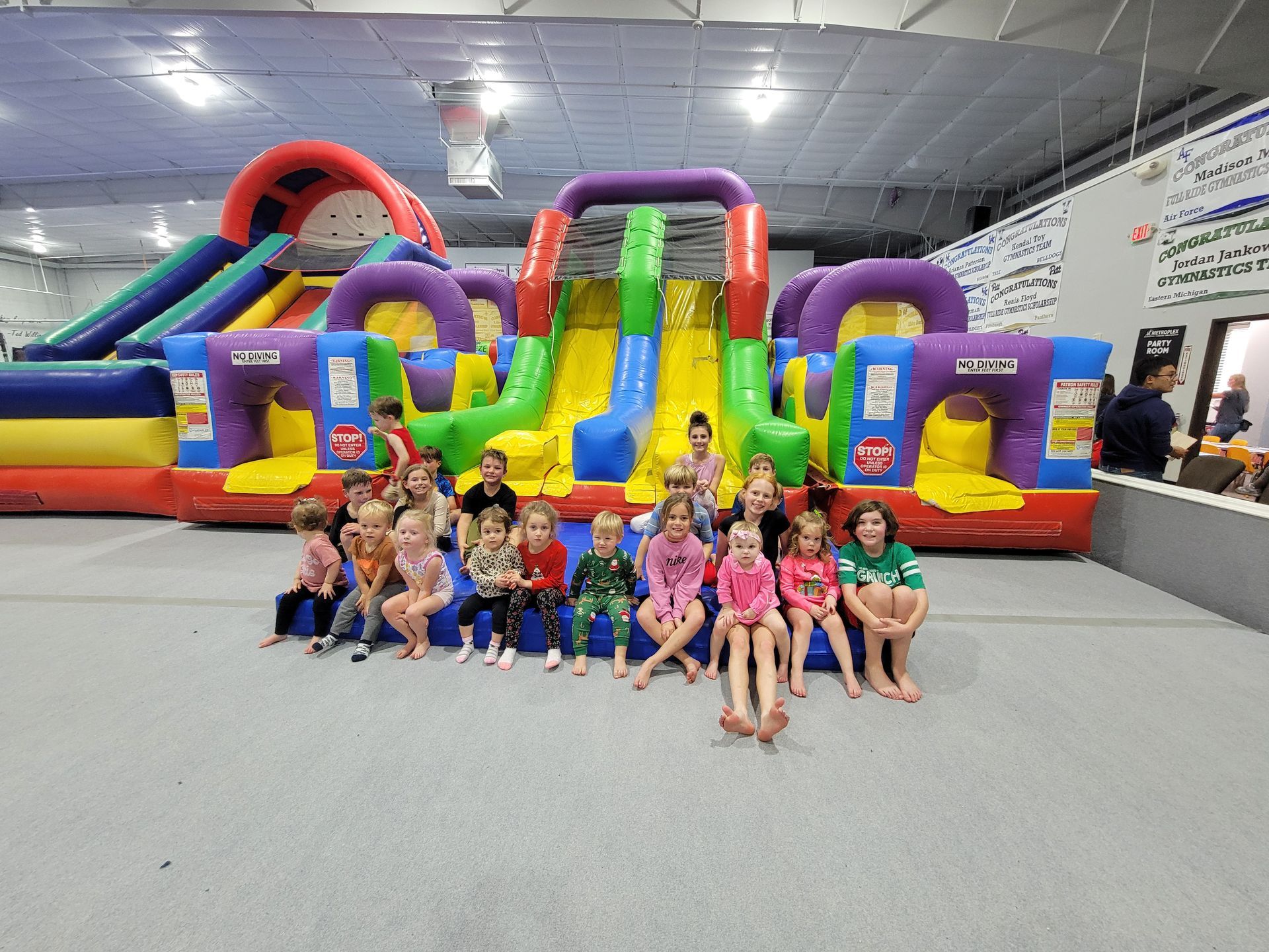 Children pose in front of a colorful inflatable obstacle course inside a gym.