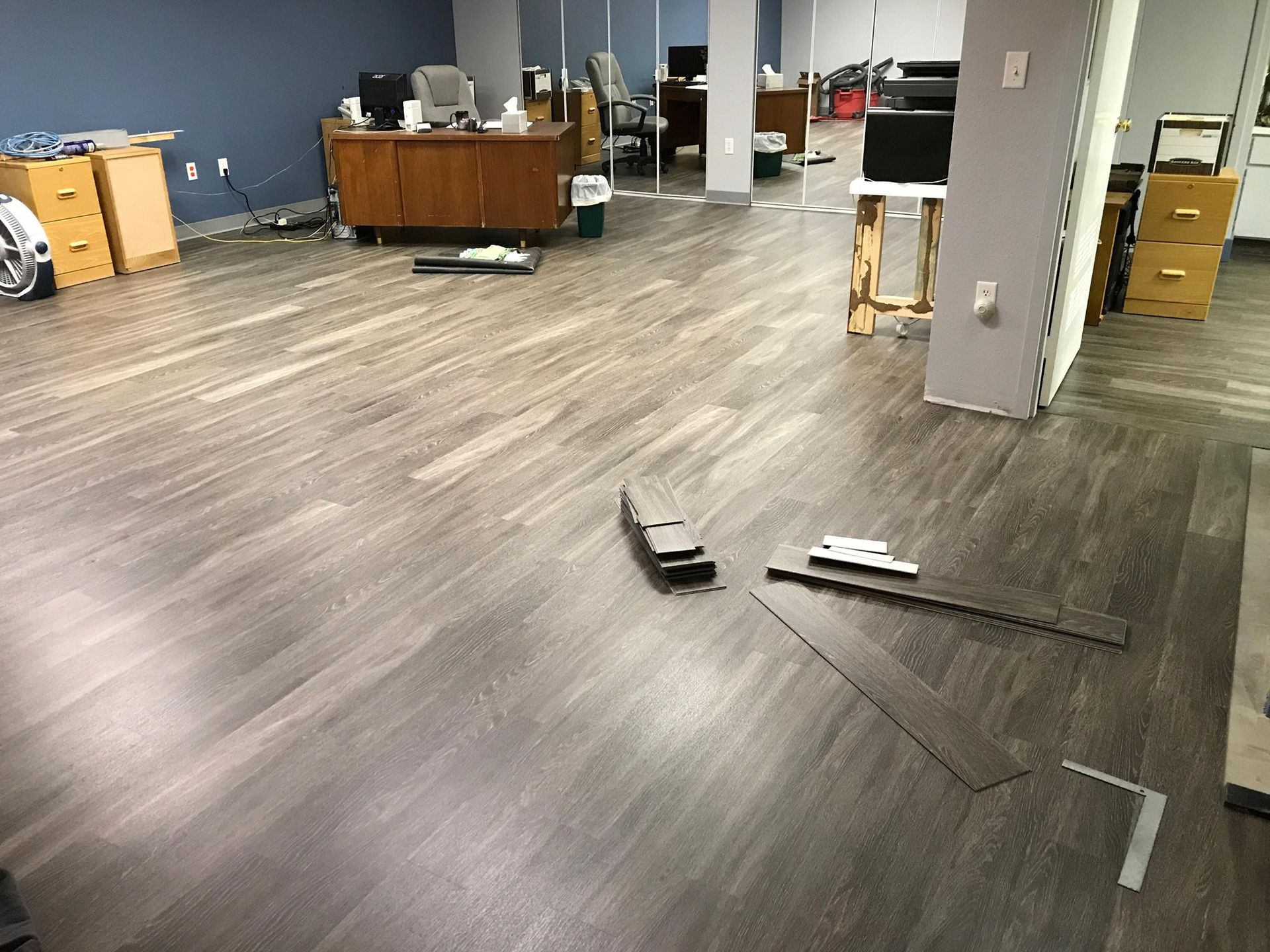 Office floor with new wood-look flooring being installed; dark gray planks on the floor, some tools