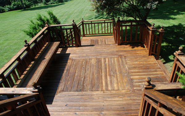Wooden deck with railing, bench, and steps; view overlooking a green lawn and trees.