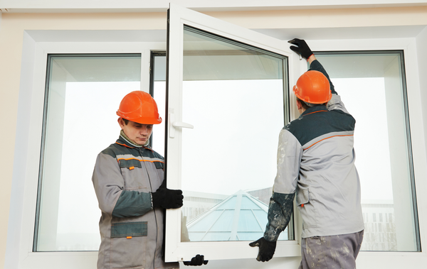 Two workers in orange hard hats install a window.