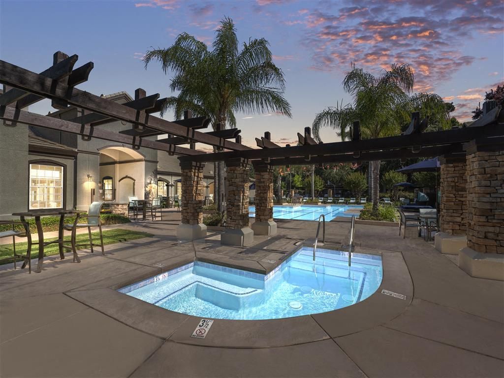 Outdoor pool area with a hot tub, palm trees, and lounge seating at an apartment community.