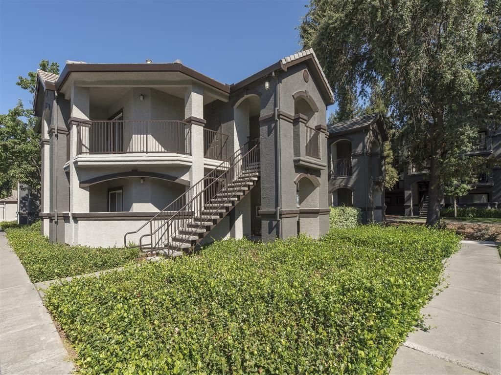 Exterior view of a gray multi-family building with stairs and landscaped hedges.