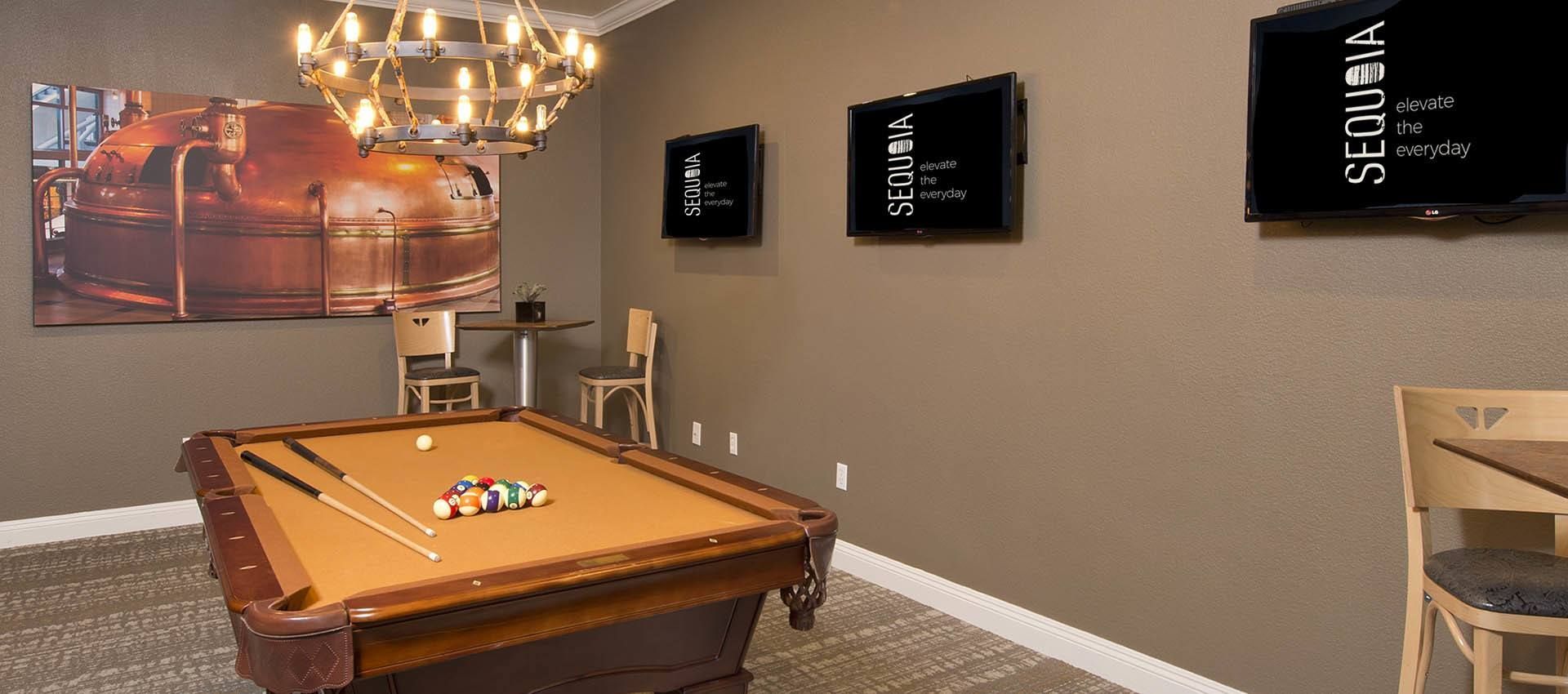 A game room with a pool table, wall-mounted TVs, and a large metal brewing tank art piece.