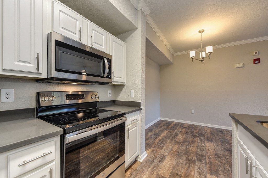 Kitchen in an apartment with white cabinets, stainless steel microwave and stove, and wood-look flooring.
