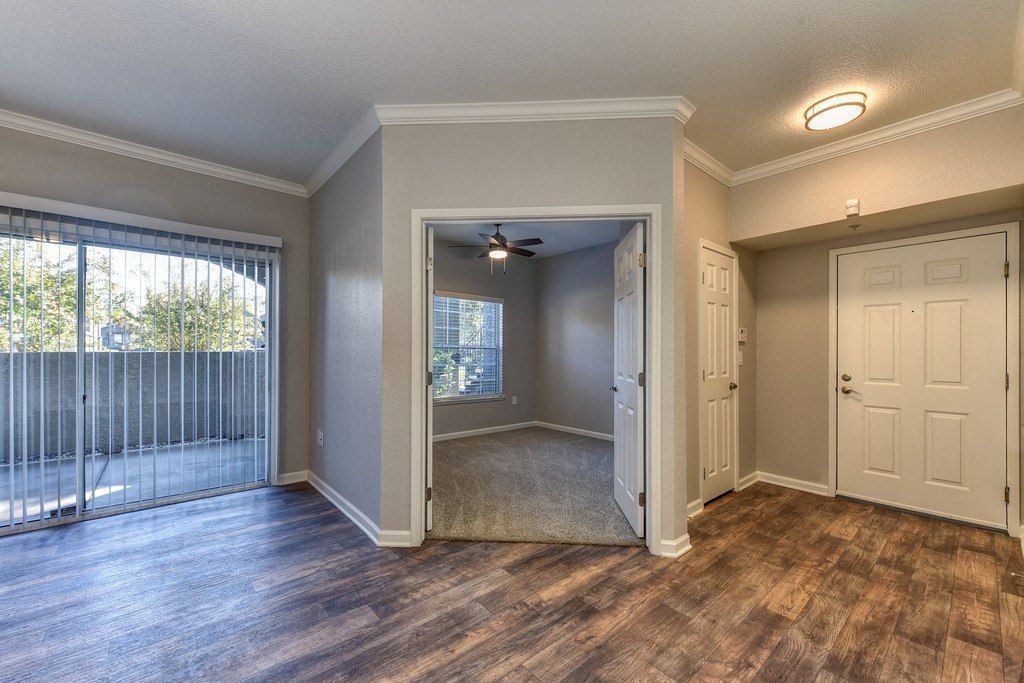 Living area with laminate flooring, sliding door to balcony, and a carpeted room near the entry.