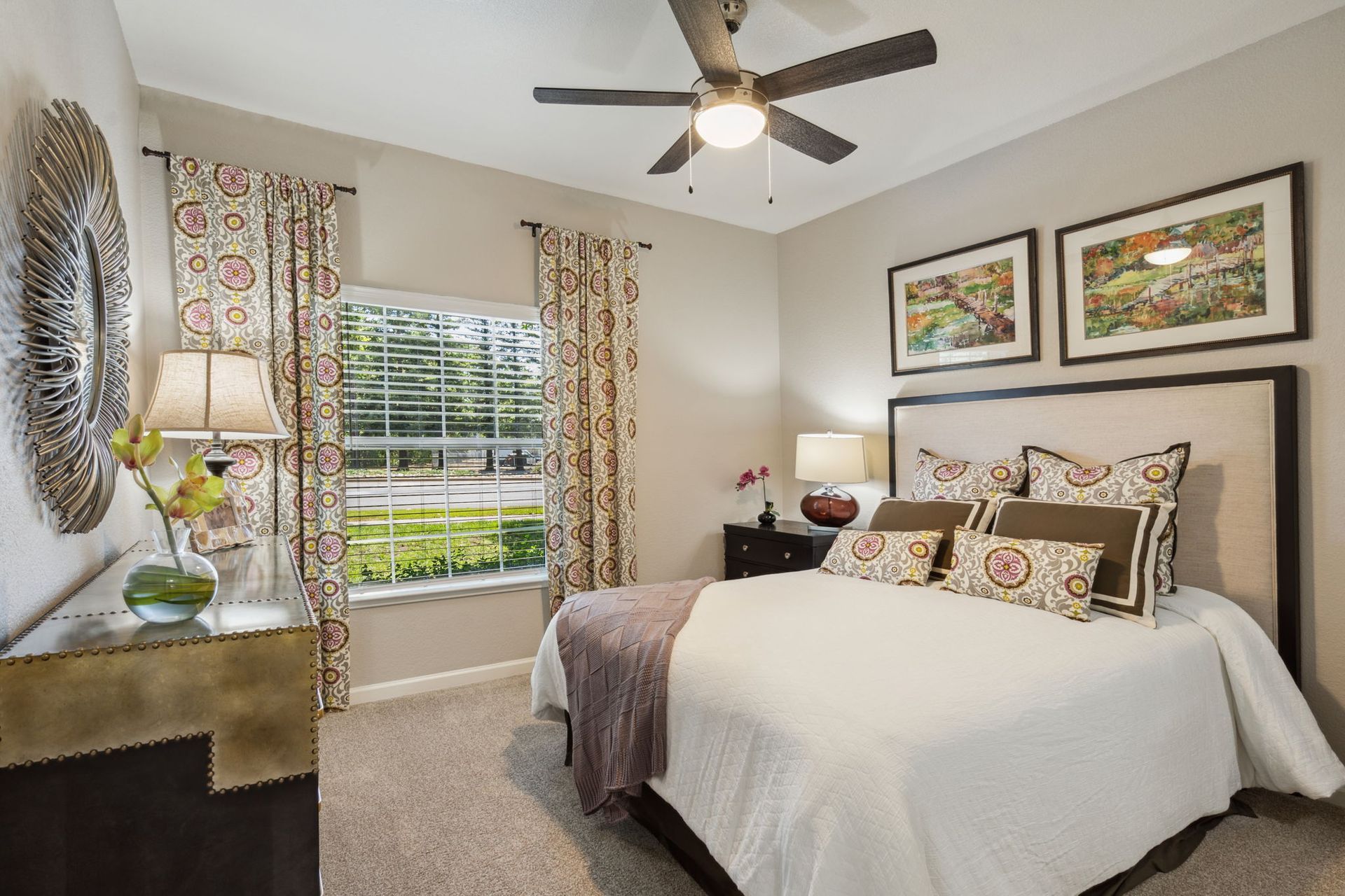 Bedroom with a bed, nightstand, and window with patterned curtains; neutral walls and carpet.