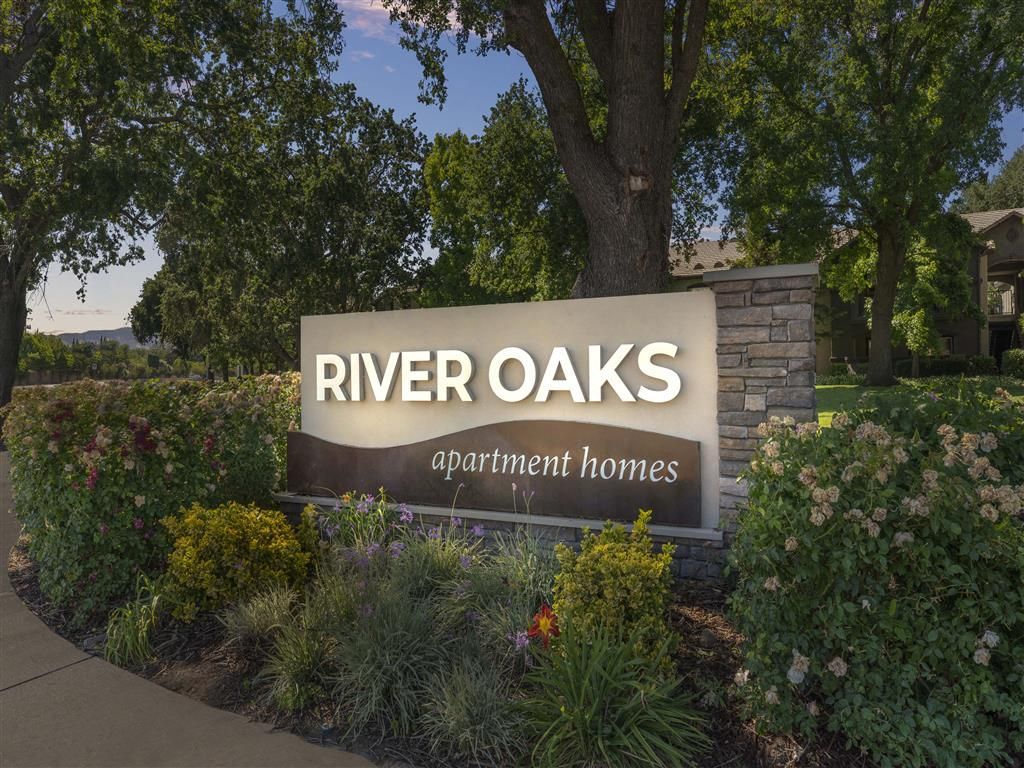 Exterior entrance sign for River Oaks apartment homes with landscaping.