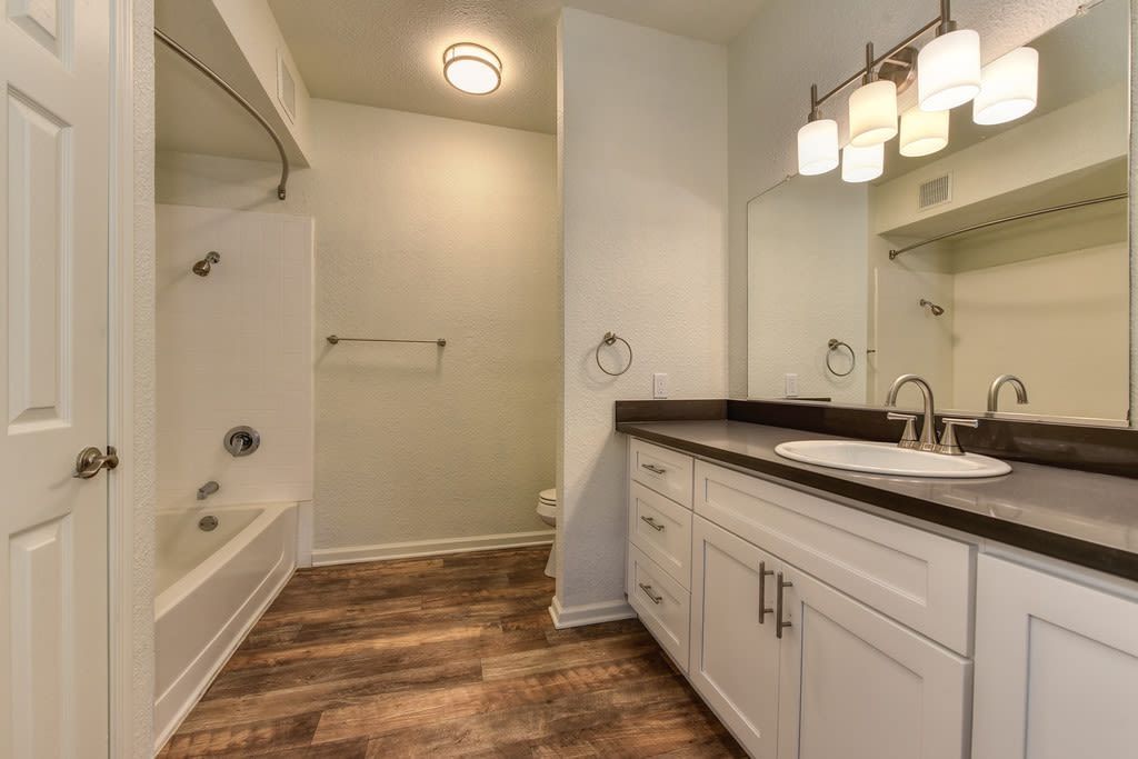 Bathroom with white cabinetry, brown countertop, brown flooring, tub/shower combo.