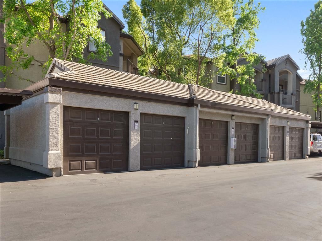 Row of brown garage doors at a multi-family complex with trees above.