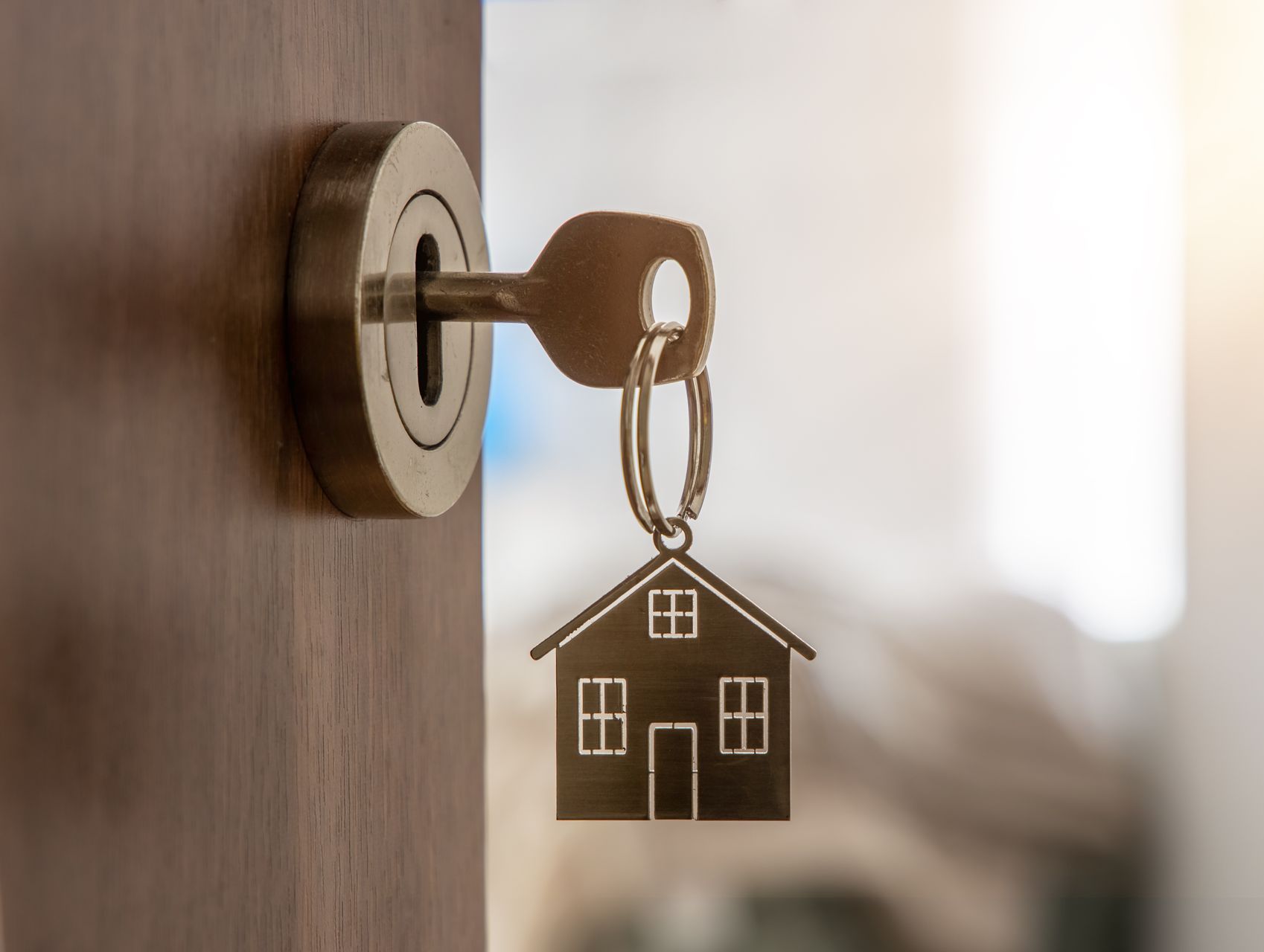 A key is hanging in a door lock with a house keychain.