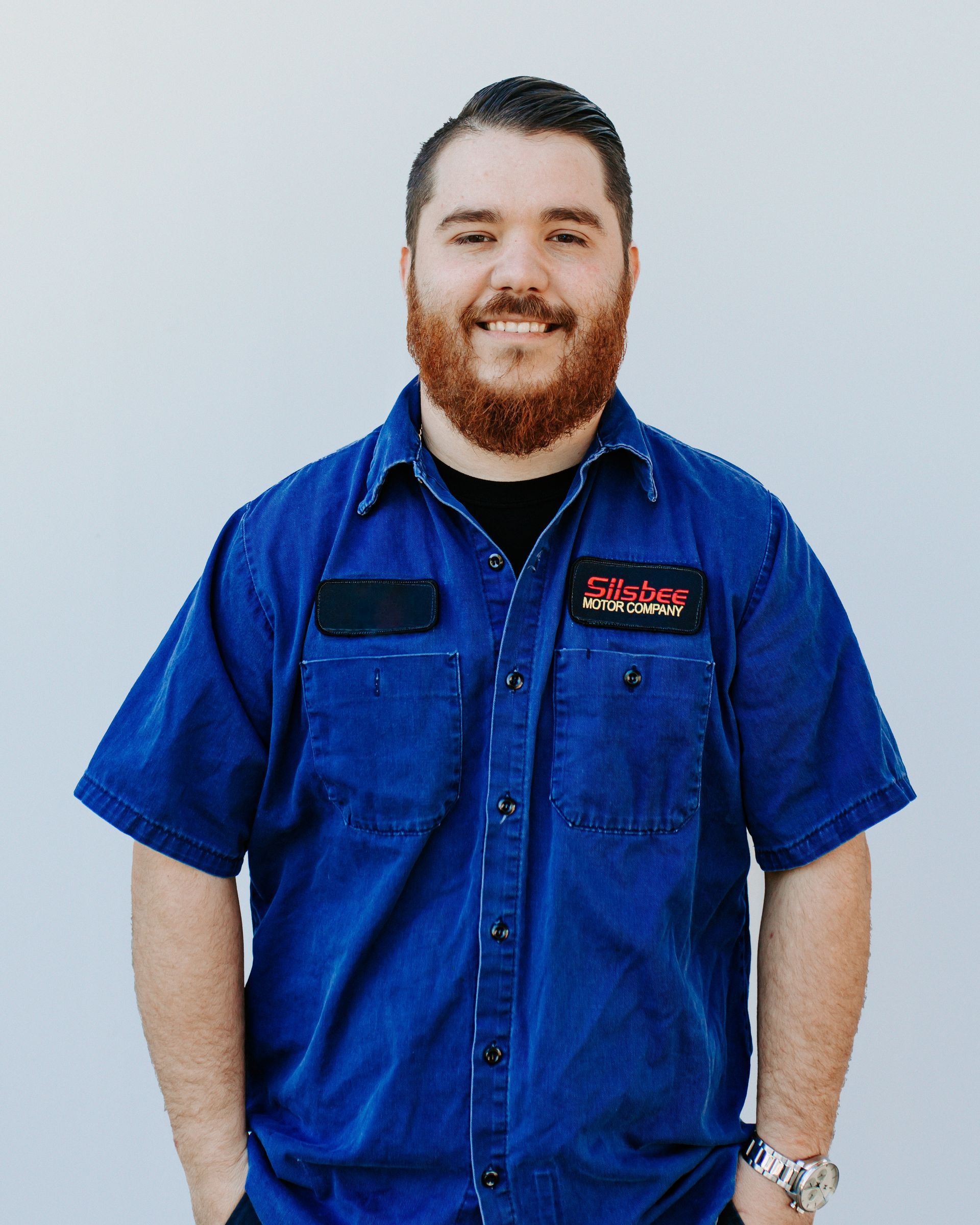 A man with a beard is wearing a blue shirt and smiling.