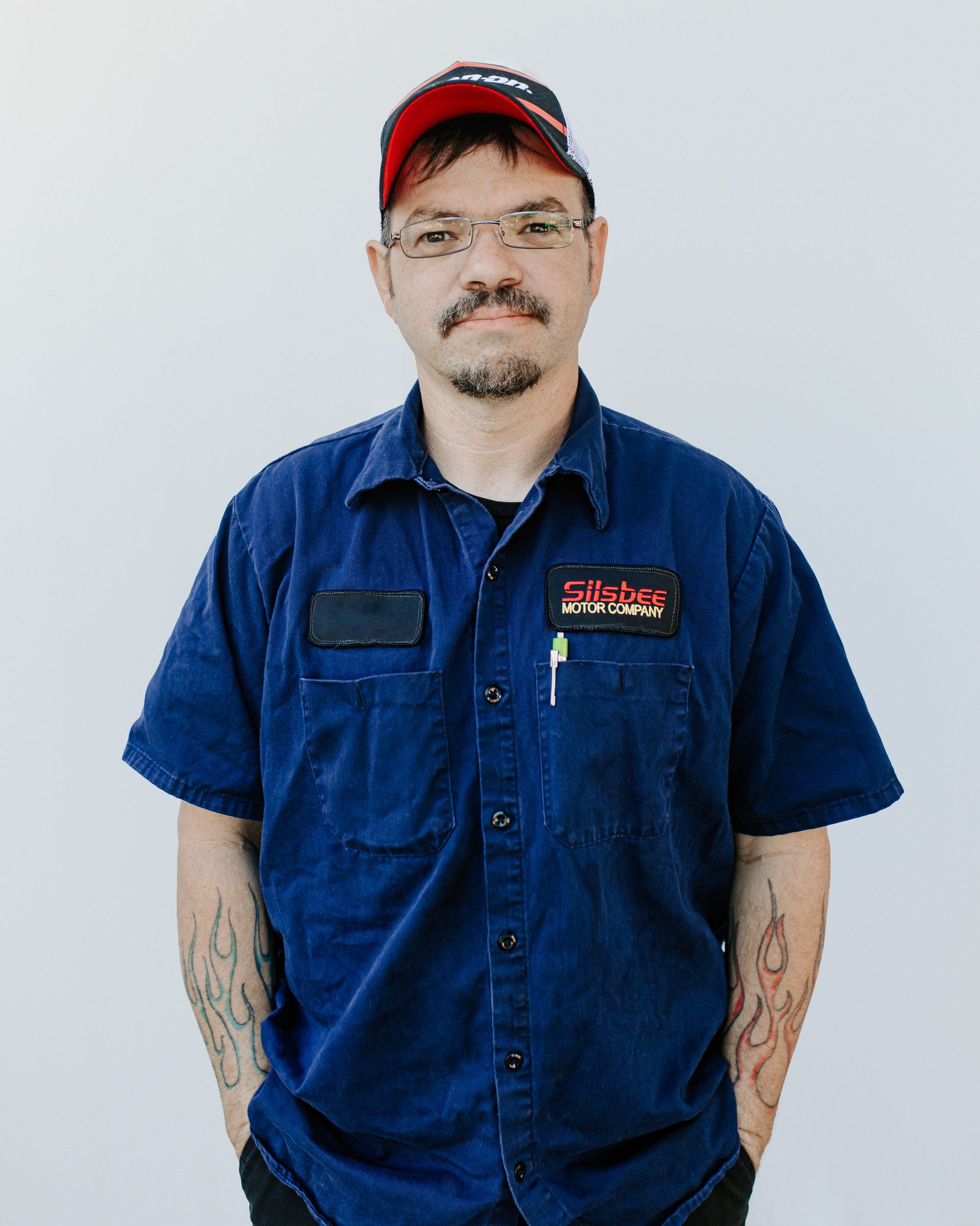 A man wearing a blue shirt and a red hat is standing with his hands in his pockets.