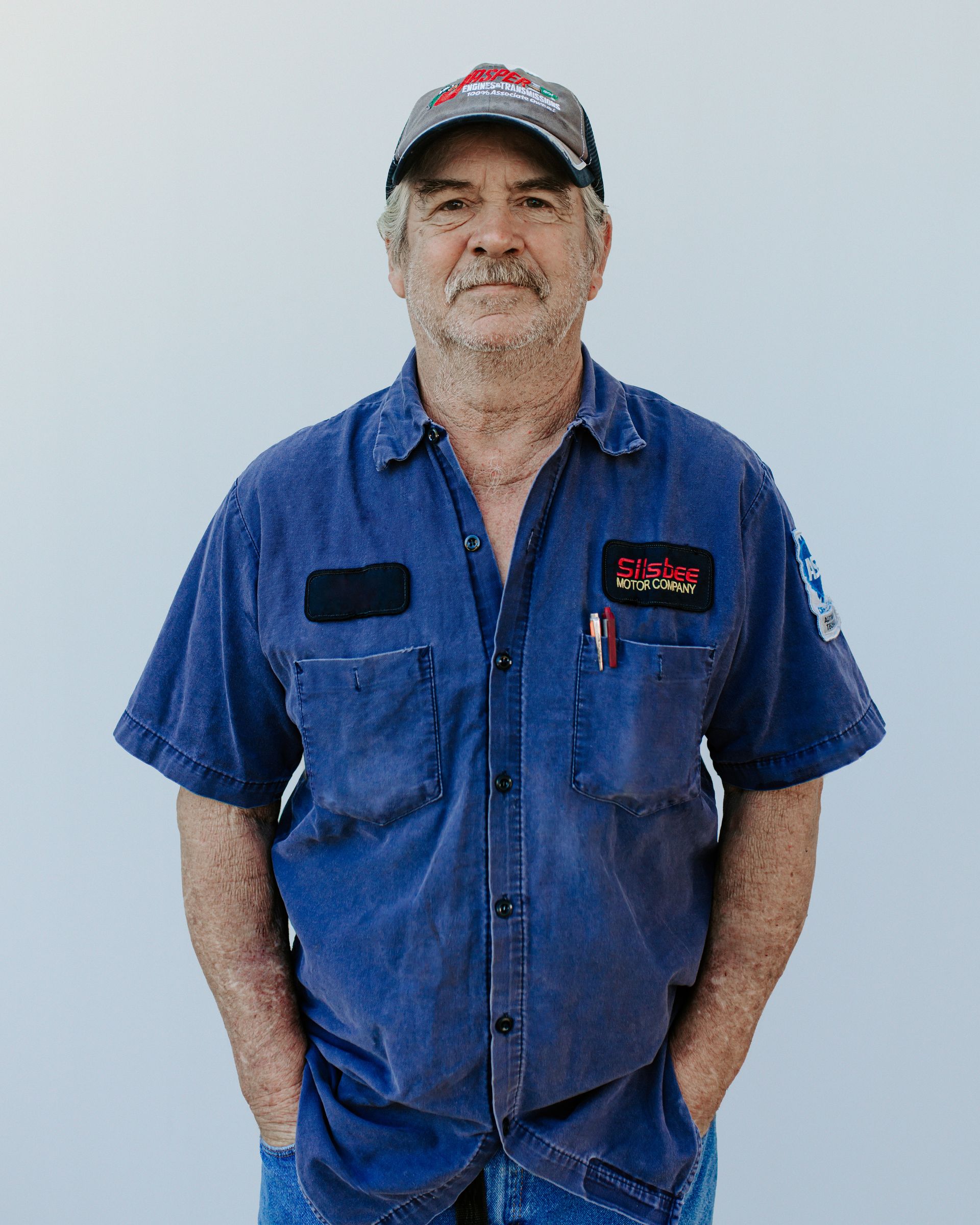 A man in a blue shirt and hat is standing with his hands in his pockets.