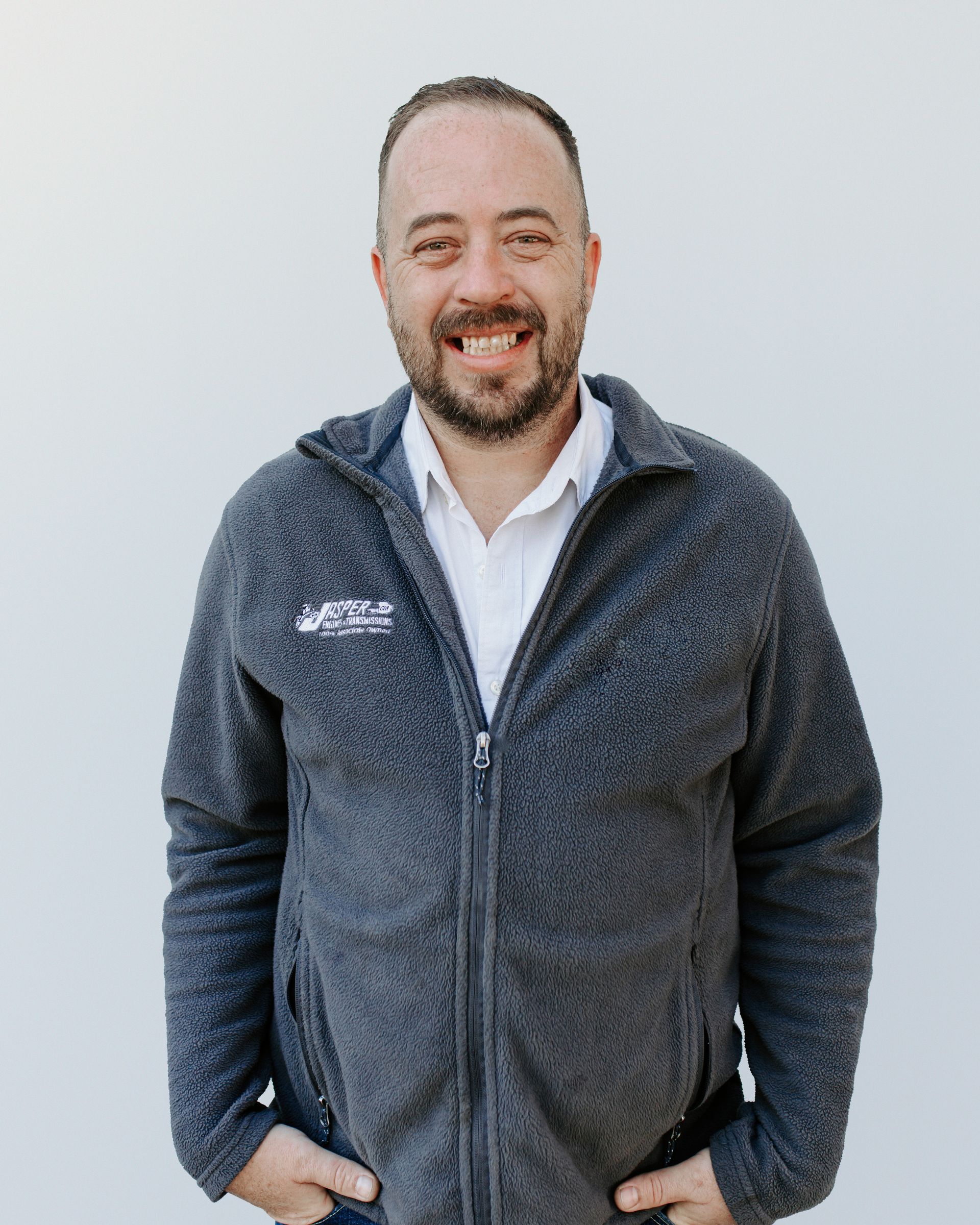 A man with a beard is wearing a gray jacket and smiling.