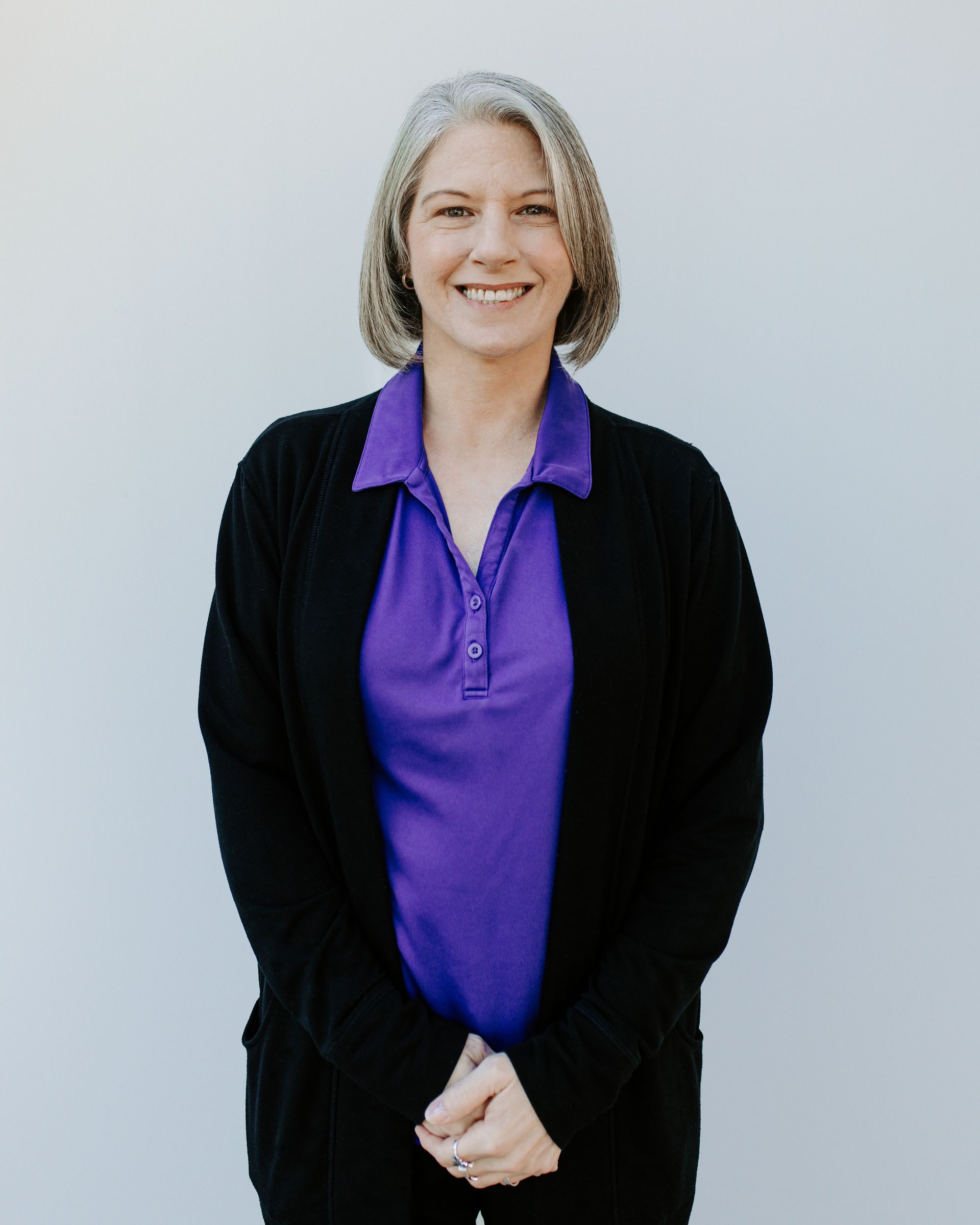 A woman wearing a purple shirt and a black cardigan smiles for the camera