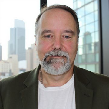 Head-and-shoulders portrait of a man in a blazer and white shirt with a city skyline behind him