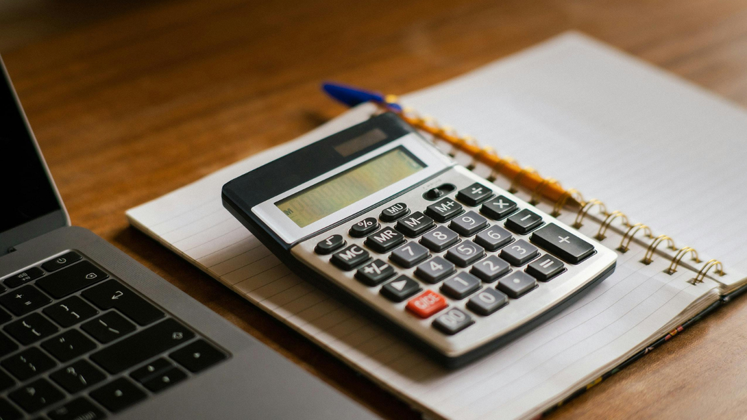 Calculator on a notebook beside a laptop keyboard on a wooden desk