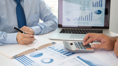 Business meeting with charts, a laptop, and a calculator as two people review financial documents.