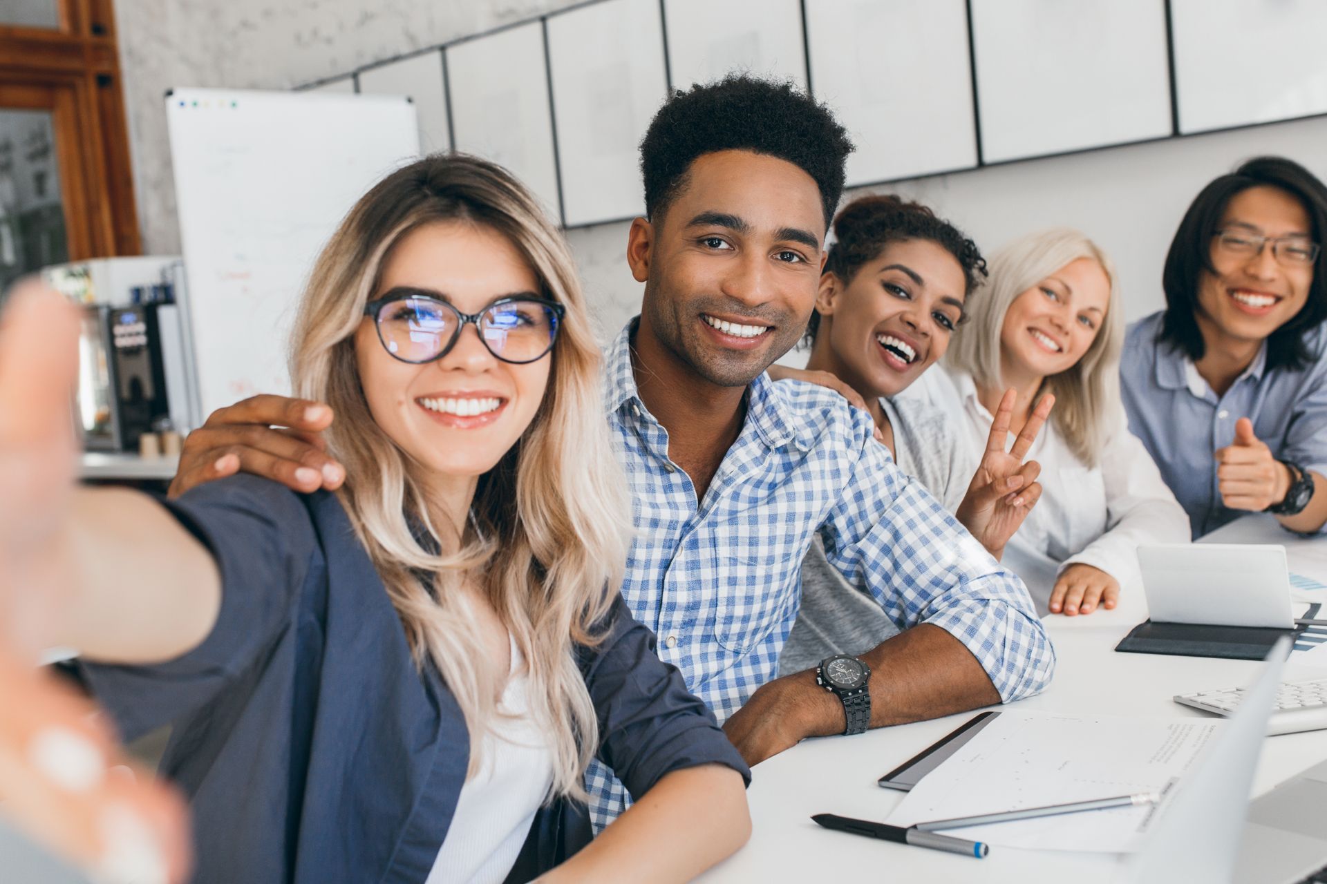Cinq collègues prennent un selfie dans une salle de conférence lumineuse.
