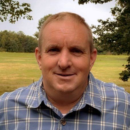 A man in a plaid shirt is smiling in front of a field