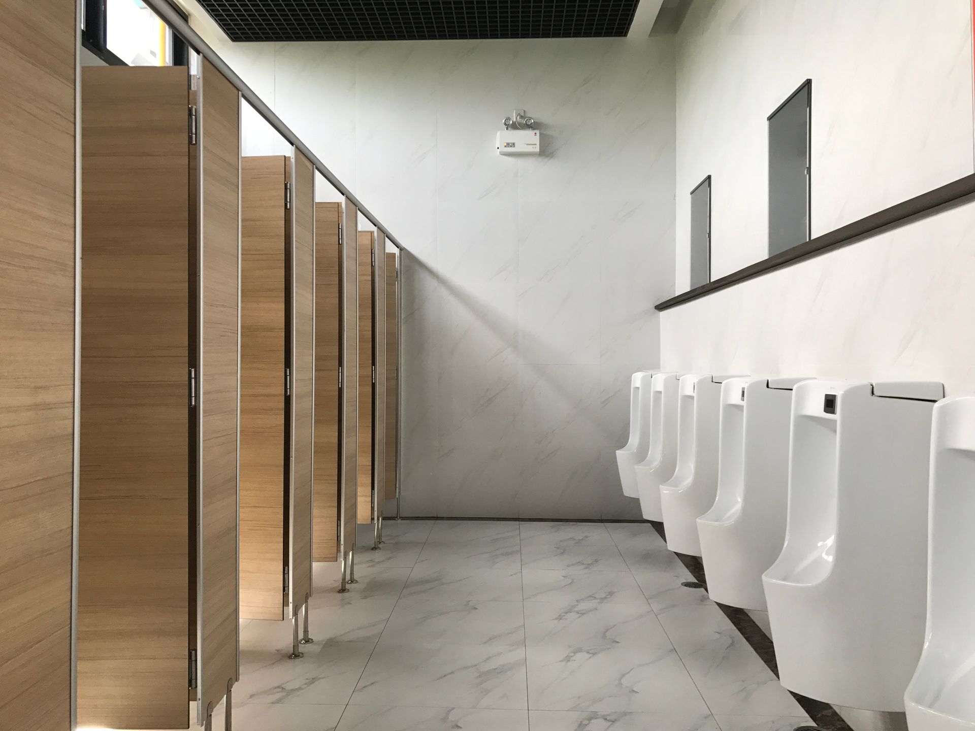 A row of urinals in a public restroom with wooden stalls.